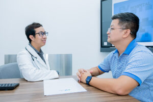 An FV Hospital doctor in a white coat consulting with a patient across a desk